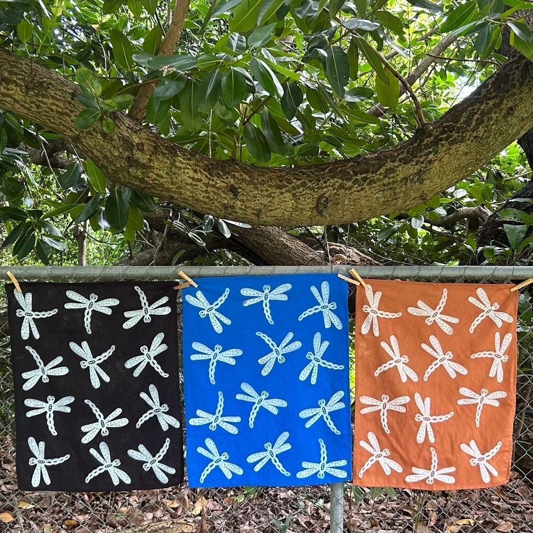 Three tea towels, lino printed with dragonflies hang on a fence.